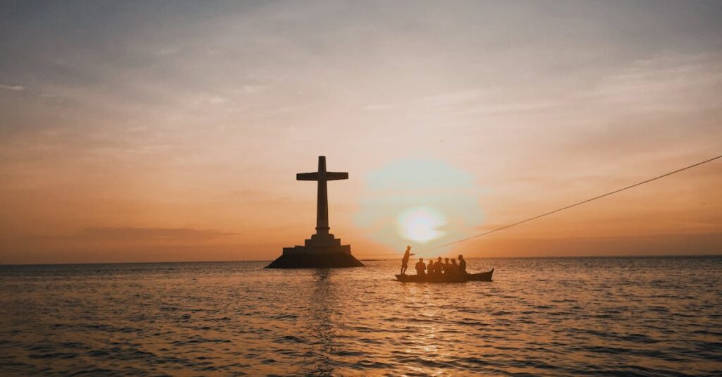 A striking silhouette of a cross and boat against a vibrant sunset over the sea.
